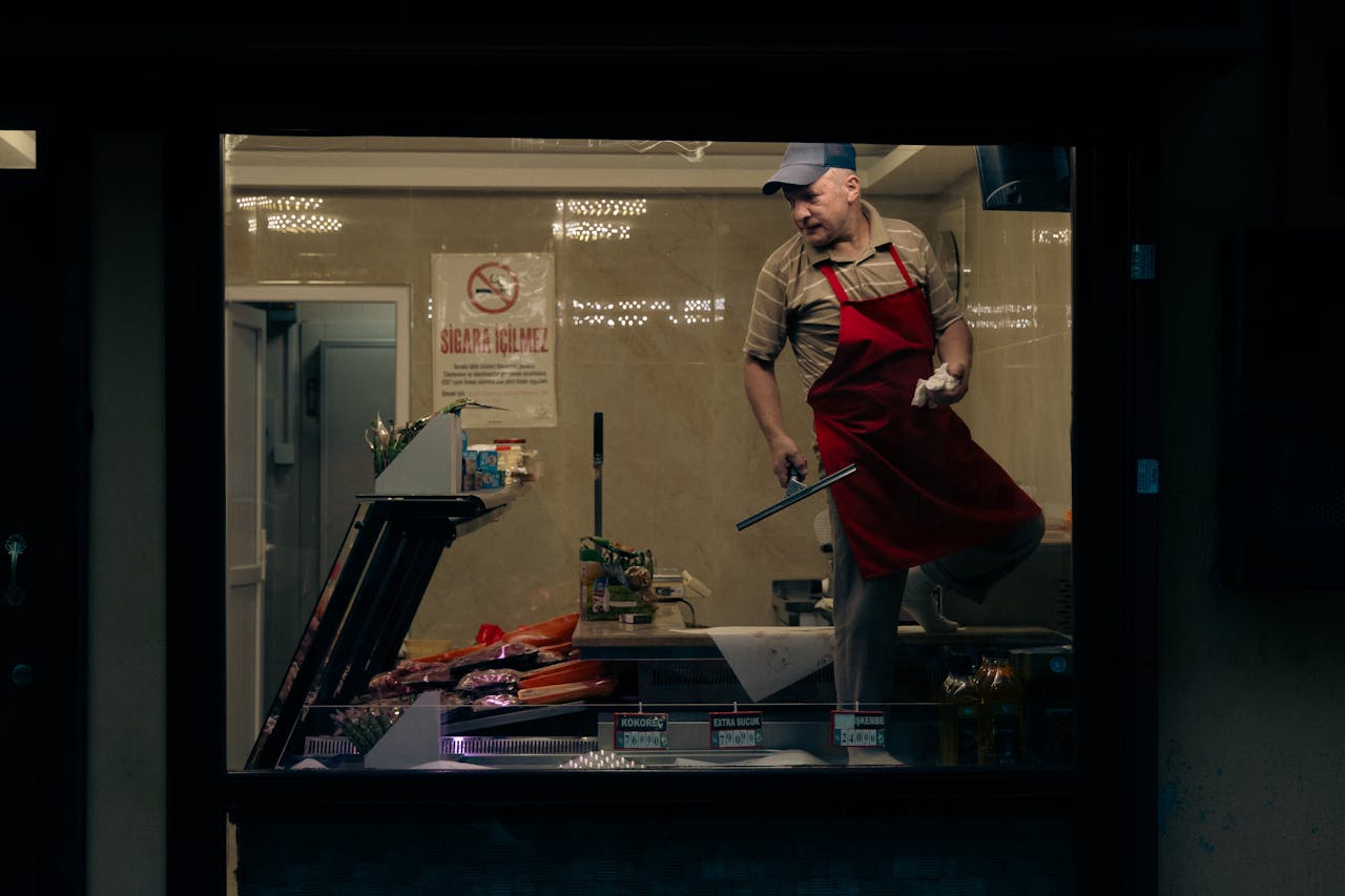 A butcher inside a shop in Bursa, Türkiye, wearing an apron and cap, working with meat.