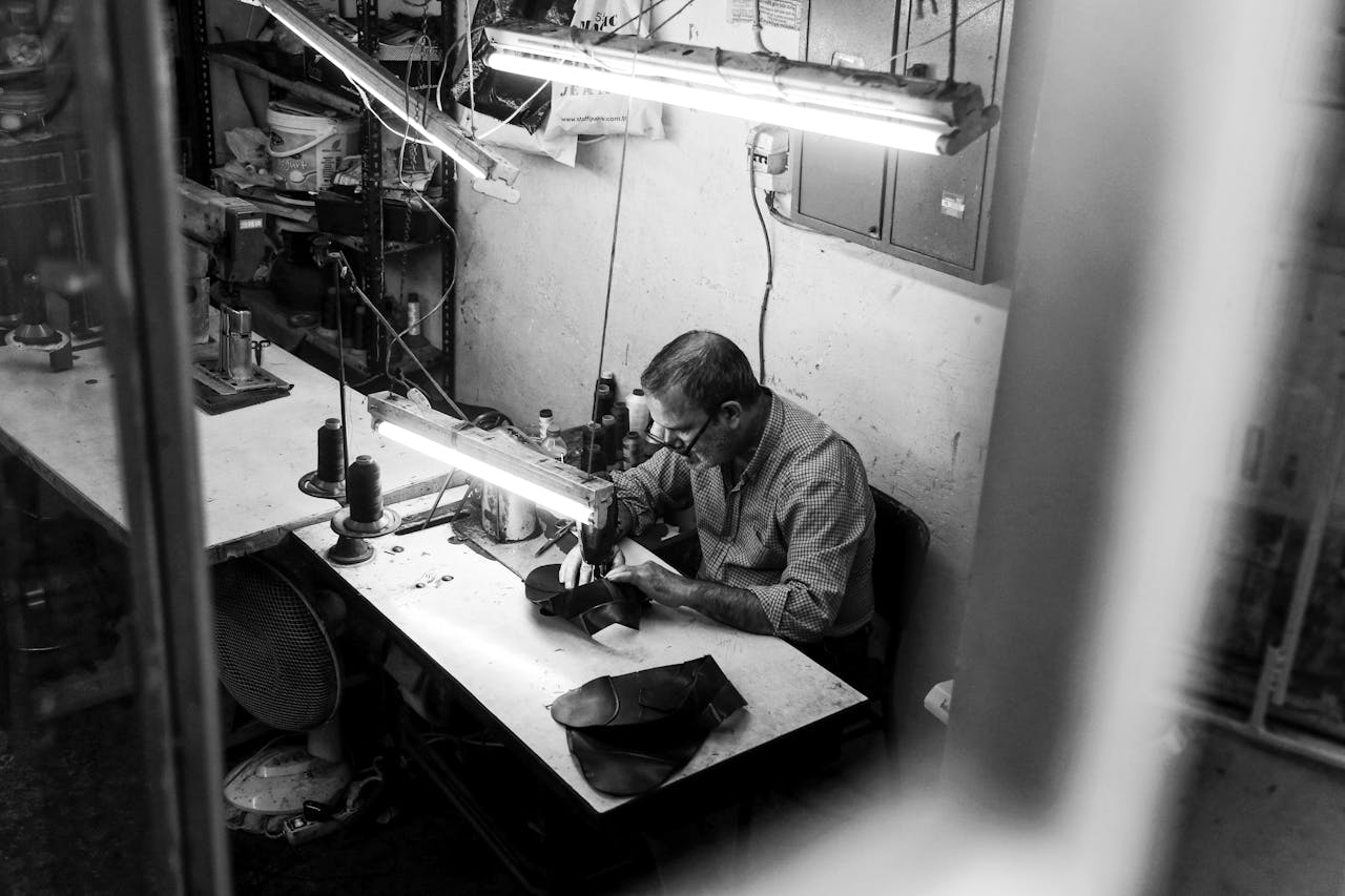 our-story-01 A focused craftsman using a sewing machine in an Istanbul workshop, captured in black and white.
